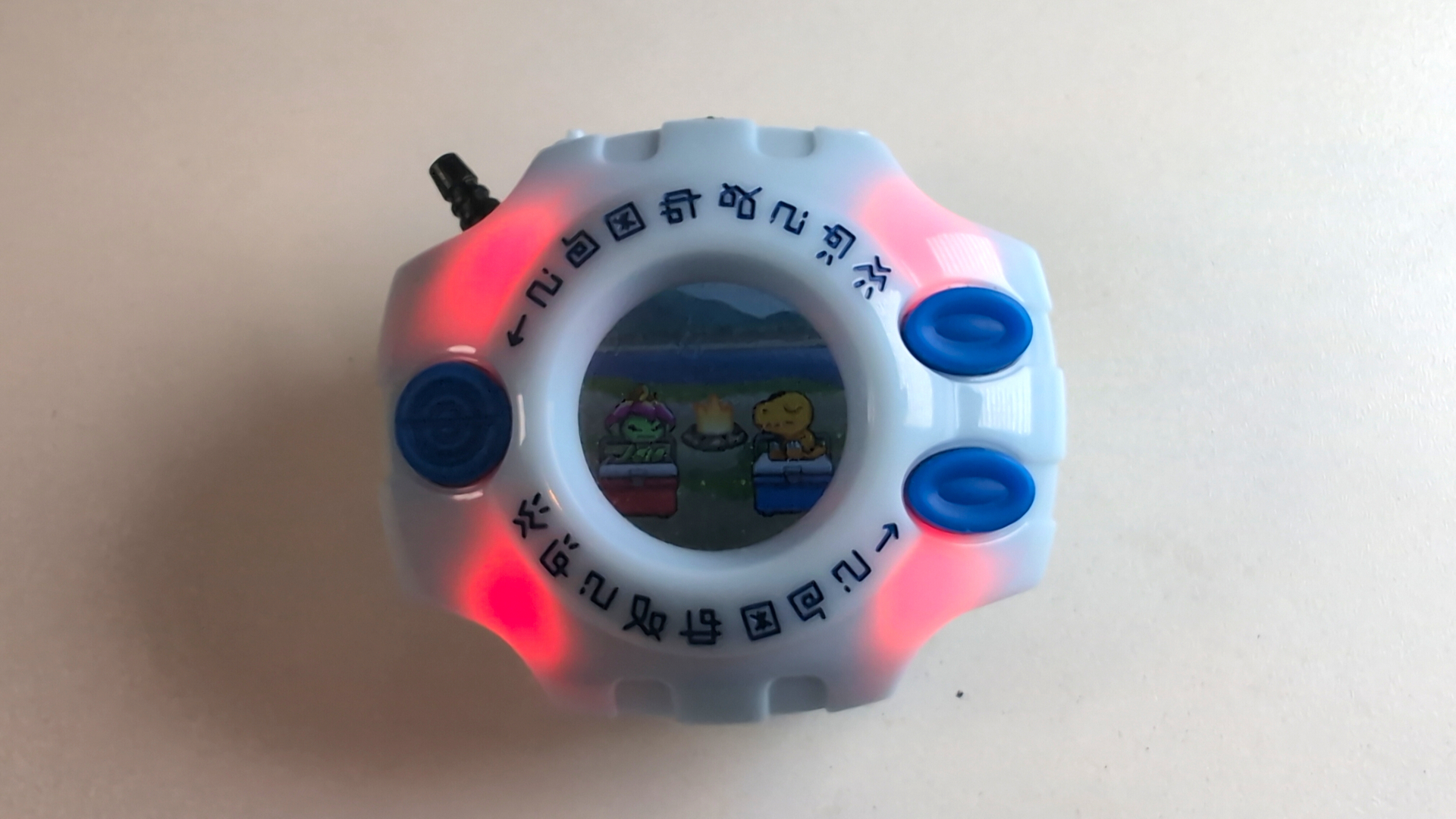 Original Digivice aus Digimon Adventure in der 25th Color Evolution Edition mit Farbdisplay, auf dem die schlafenden Digimon Agumon und Palmon zu sehen sind. Rote LED-Lichter leuchten im Inneren des orangefarbenen Geräts.