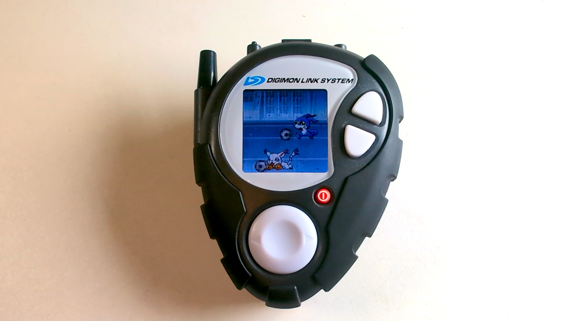 D-3 Digivice aus Digimon Adventure 02 in der 25th Color Evolution Edition mit Farbdisplay, auf dem die Digimon V-Mon und Tailmon beim gemeinsamen Ballspielen zu sehen sind.