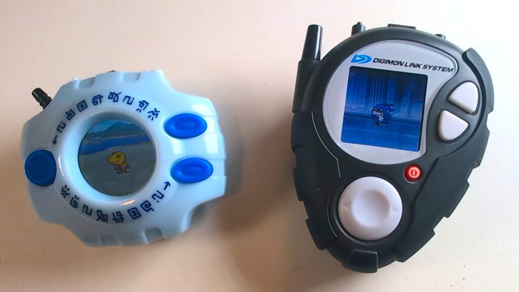 Zwei Digimon Digivices nebeneinander: Links das klassische Digivice aus Digimon Adventure und rechts das D-3 aus Digimon Adventure 02, beide in der speziellen 25th Color Evolution Edition mit detaillierten Farbdisplays.